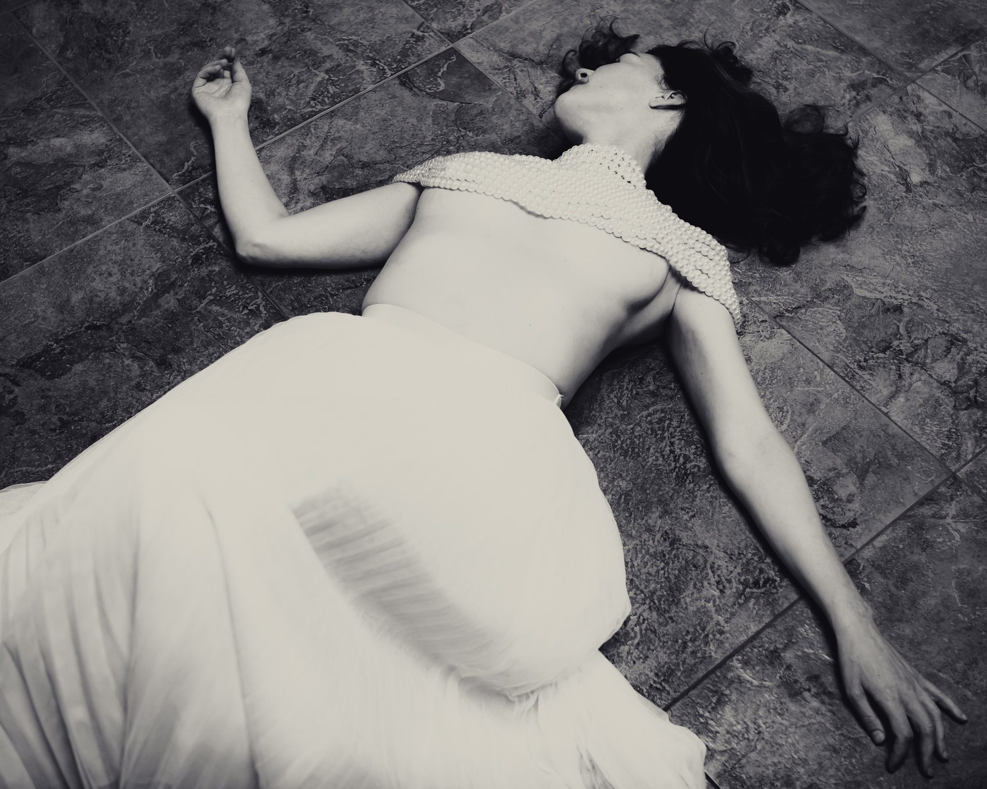 Black and white photograph of Sara Gartland lying on a stone floor in a white skirt and draped pearls